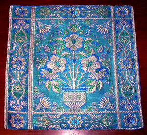 Handwoven silk placemat featuring an ornate floral medallion in a vase, framed by vine borders